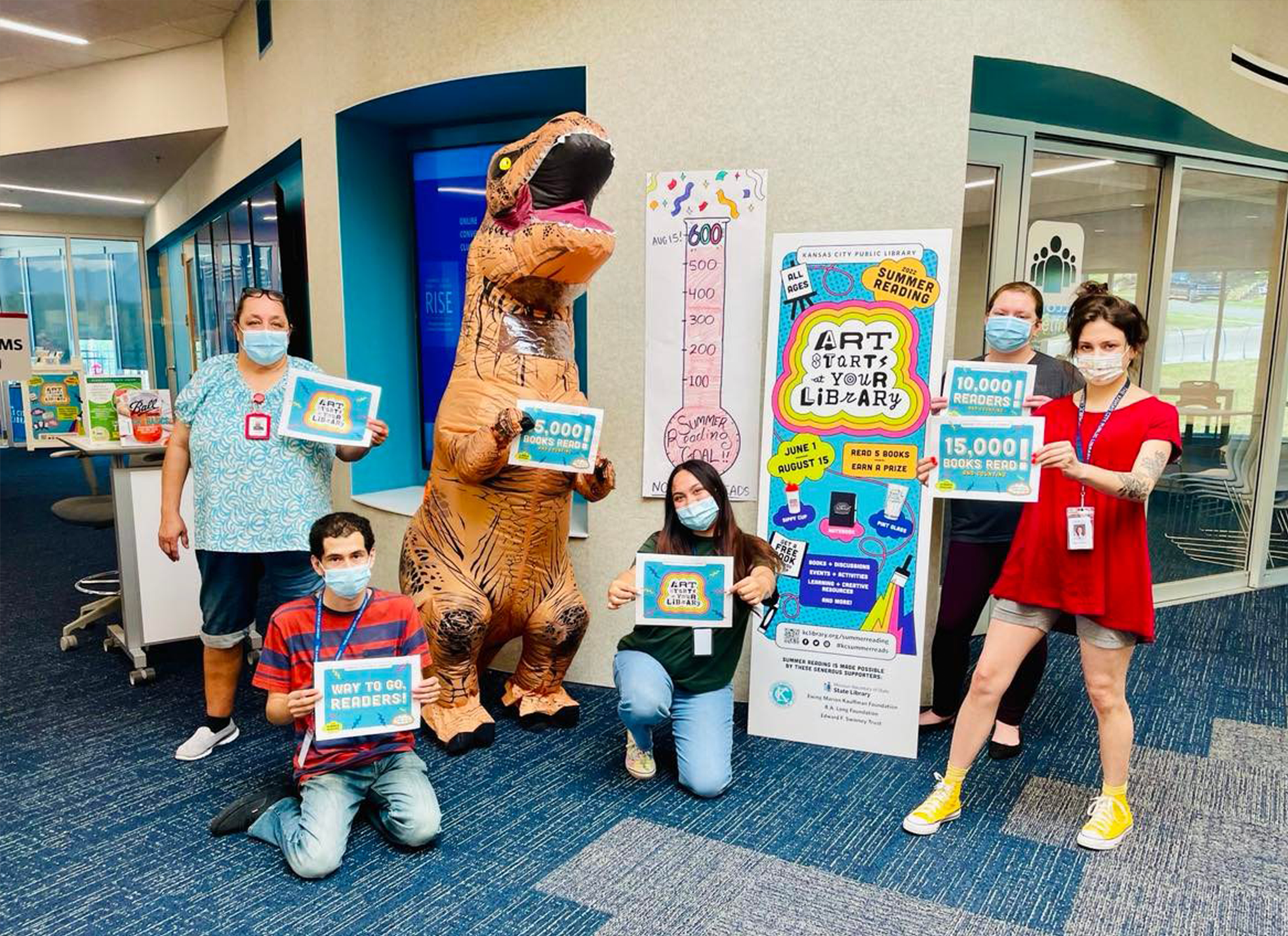 Group of library staff members and one dinosaur with signs
