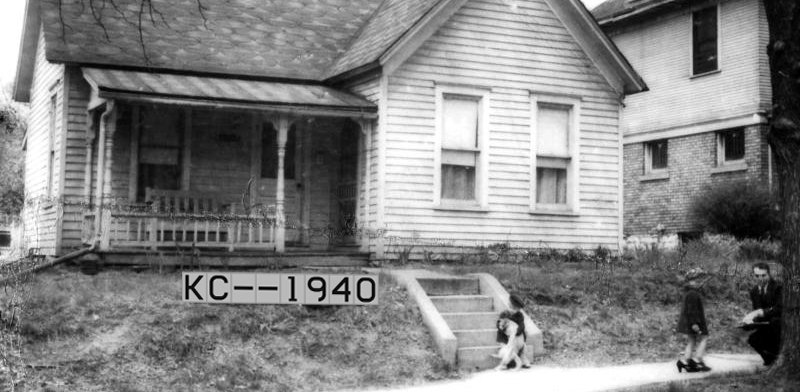 man, two children, and cat in front of house in black and white