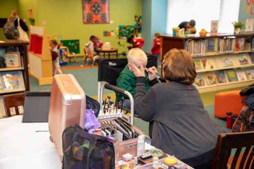 A woman applies face paint to a child at the Central Library.