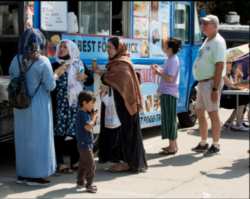 Women, children, and a man line up for a food truck in the historic NE of Kansas City on World Refugee Day.