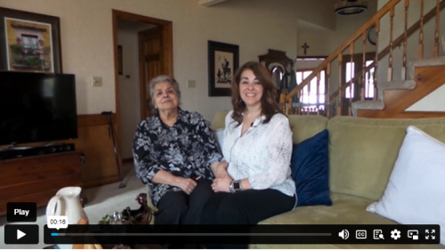 Two women sit on a couch smiling.