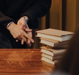 hands sitting near stack of books with audience