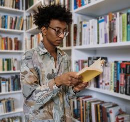 Teen reading book in front of book shelves
