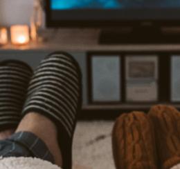 two adults wearing slippers propped up watching TV