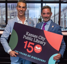 two men in blue suits hold giant library card