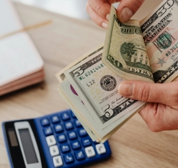 money in hands, calculator and clipped paper on table