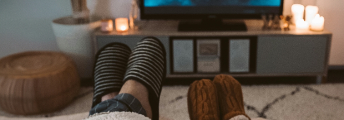 two adults wearing slippers propped up watching TV