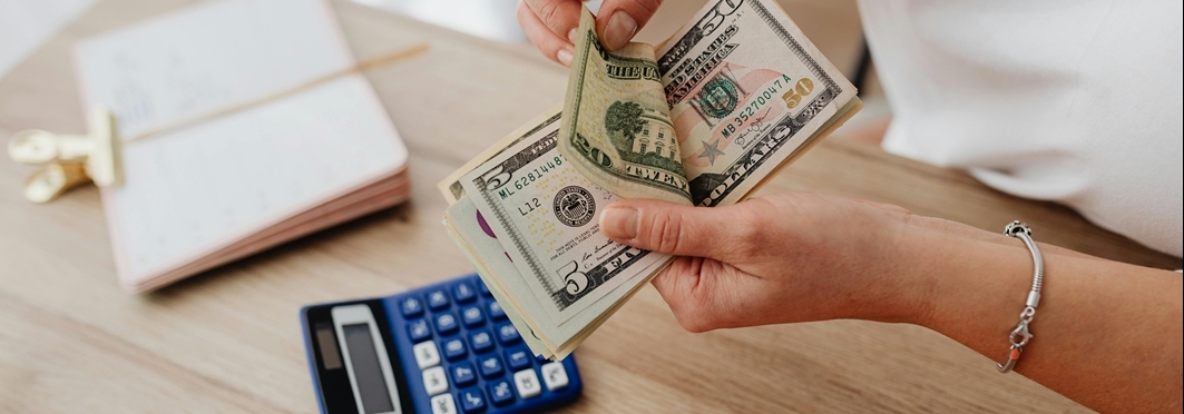money in hands, calculator and clipped paper on table