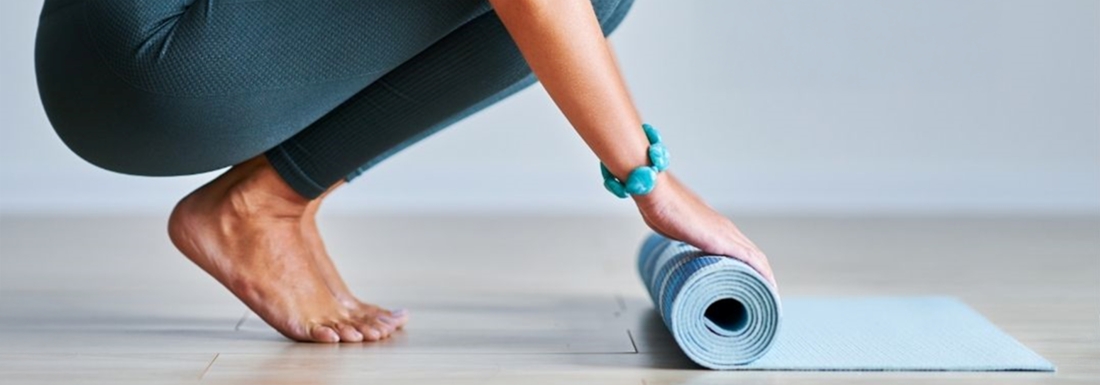 woman crouching rolling up yoga mat