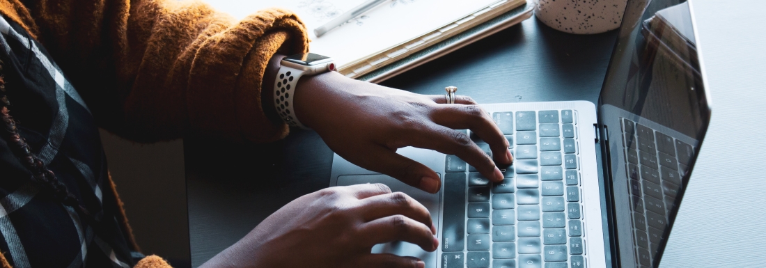 person typing on laptop next to coffee mug and notebook with pen