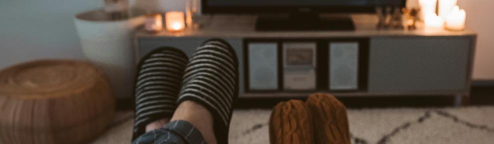 two adults wearing slippers propped up watching TV