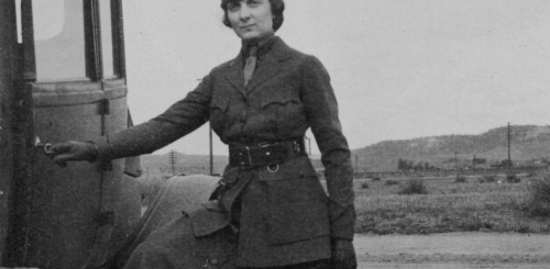 Black and white photo of a woman in uniform standing outside a vehicle.