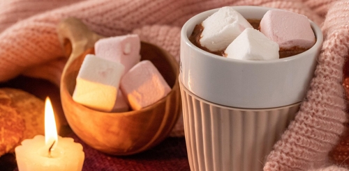 hot chocolate in blanket next to candle and marshmallows