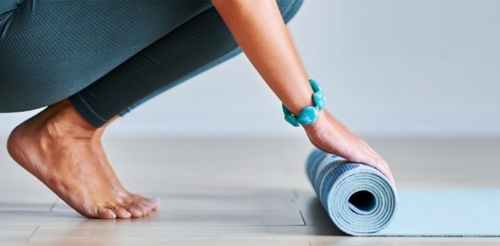 woman crouching rolling up yoga mat