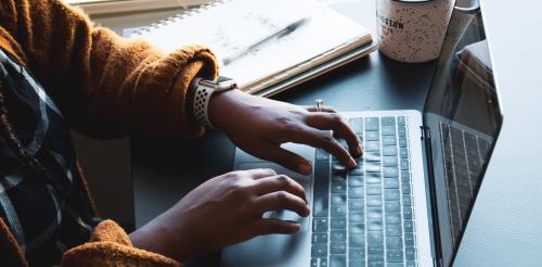 person typing on laptop next to coffee mug and notebook with pen